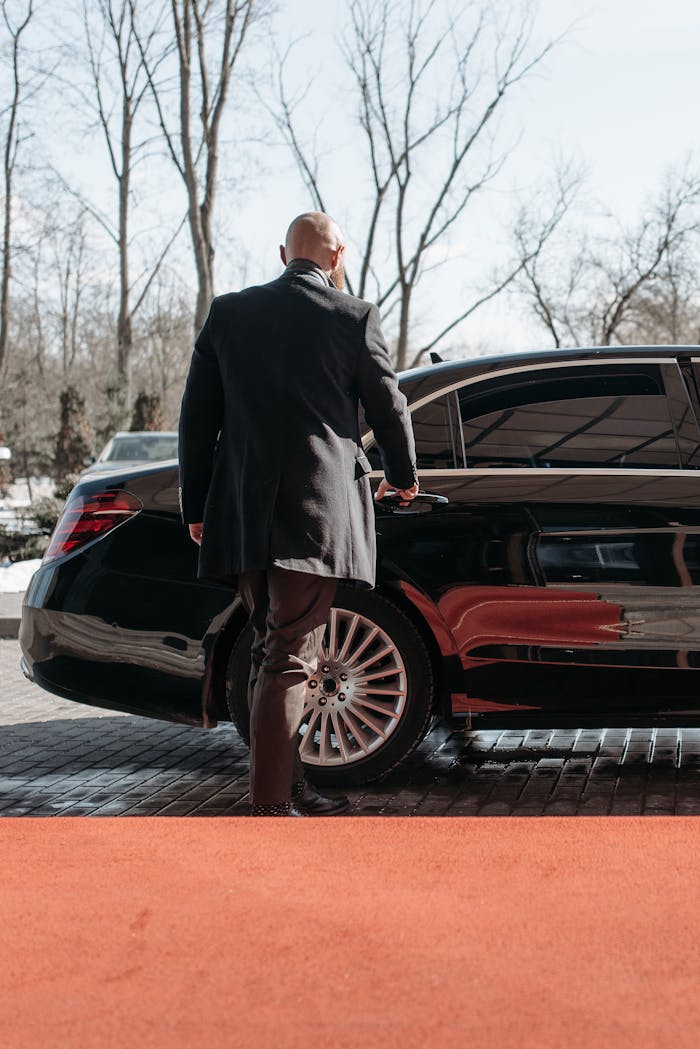 gallery-2 Bald man in a black suit approaches a luxury black car on a sunny day.