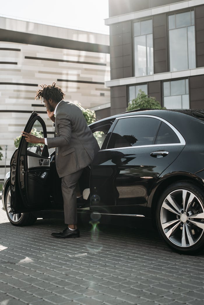gallery-4 Stylish adult man in gray suit stepping out of a luxury black car in a modern city environment.