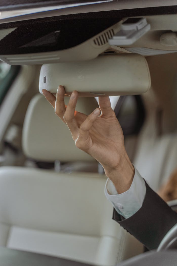 gallery-6 A professional chauffeur in a suit adjusting the rear-view mirror in an elegant car interior, focusing on precision and safety.